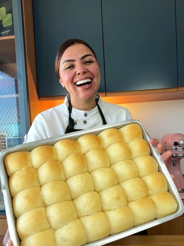 Chef Geicy Galindo segurando uma bandeja de pãezinhos dourados recém-assados